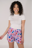A woman wearing a white t-shirt and purple boxer shorts with a multicolored heart pattern.