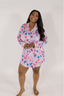 A woman modeling a purple sleep dress with a jewel pattern. The dress has a classic PJ silhouette with long sleeves and a button-up front.