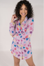A woman modeling a purple sleep dress with a jewel pattern. The dress has a classic PJ silhouette with long sleeves and a button-up front.