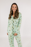 A woman wearing a long sleeve and pant pajama set with a green background and champagne glass pattern.