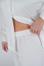 A woman modeling a white feather long sleeve and cropped pant pajama set with detachable feather cuffs on the wrists and ankles.