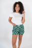 A woman wearing a white t-shirt and green boxer shorts with a geometric bow pattern.