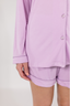 A woman wearing a long sleeve and short lavender pajama set with a button-up front and a collar.
