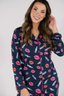 A woman wearing a navy long sleeve pajama top with a lipstick print design, paired with matching pants, standing against a white background.