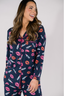 A woman wearing a navy long sleeve pajama top with a lipstick print design, paired with matching pants, standing against a white background.