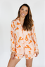 Woman wearing a peach-colored pajama set with orange animal prints on a white background