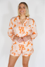 Woman wearing a matching pajama set with orange and beige pattern on a white background