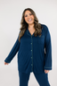 A woman wearing a long sleeve navy blue pajama set with empire green piping and a collar.