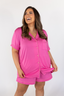A woman wearing a petal pink short sleeve and short pajama set with a smiling expression.