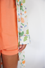 Person wearing an orange outfit with a floral-patterned garment partially visible.