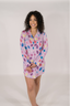 A woman modeling a purple sleep dress with a jewel pattern. The dress has a classic PJ silhouette with long sleeves and a button-up front.