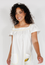 Woman wearing a white dress with yellow trim and a lemon design on a plain background
