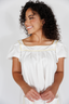 Woman wearing a white dress with yellow trim against a plain background
