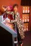 Woman in luxury leopard print robe standing next to a jukebox with bowling pins in the background. 