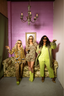 Three women in colorful luxury pajamas posing in a room with a purple wall and chandelier.