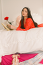 Woman in red outfit holding a rose and a book on a bed