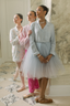 Three ballerinas in a ballet studio, with one in a light blue dress and pink tights, another in a pink outfit, and the third in a white outfit.