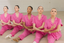 Five dancers in matching pink pajamas sitting on a wooden floor.