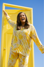 A woman standing in a yellow doorframe wearing a modal pajama set in yellow blooms.