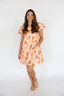 Woman wearing an orange and white patterned dress on a white background