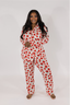 A woman wearing a long sleeve and pant pajama set with a red rose pattern on a white background.