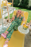 Woman in a green floral pajama set sitting on a yellow lounge chair outdoors.