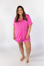 A woman wearing a petal pink short sleeve and short pajama set with a smiling expression.
