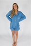 A woman wearing a long sleeve, short pajama set in a dusty blue color with white trim and a pocket on the chest.