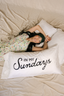 Woman lying on a bed with a pillow that says 'In My Sundays' on a beige background