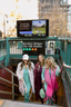 Three women standing at a subway station with a screen displaying 'Brooklyn Bridge City Hall Station'.