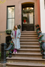 Woman in a long coat standing on a decorated staircase with a festive door in the background.