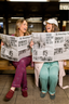 Two women reading newspapers in a subway station.