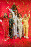 Five women in festive pajamas celebrating with confetti on a red background
