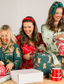 Three women preparing Christmas gifts with wrapped presents and ribbons on a table while wearing matching pajama sets