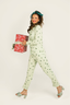 Woman in a green checkered pajama set holding a gift box against a white background