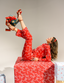 Woman in red pajama set with white patterns lying on a large wrapped gift box, surrounded by other wrapped gifts.