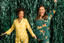 Two women posing together in front of a green tinsel background wearing matching Christmas pajamas