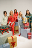 Five women in festive pajamas surrounded by Christmas presents on a white background
