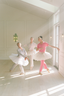Three ballet dancers in a bright, sunlit room with white walls and wooden floors dancing in luxury pajamas.